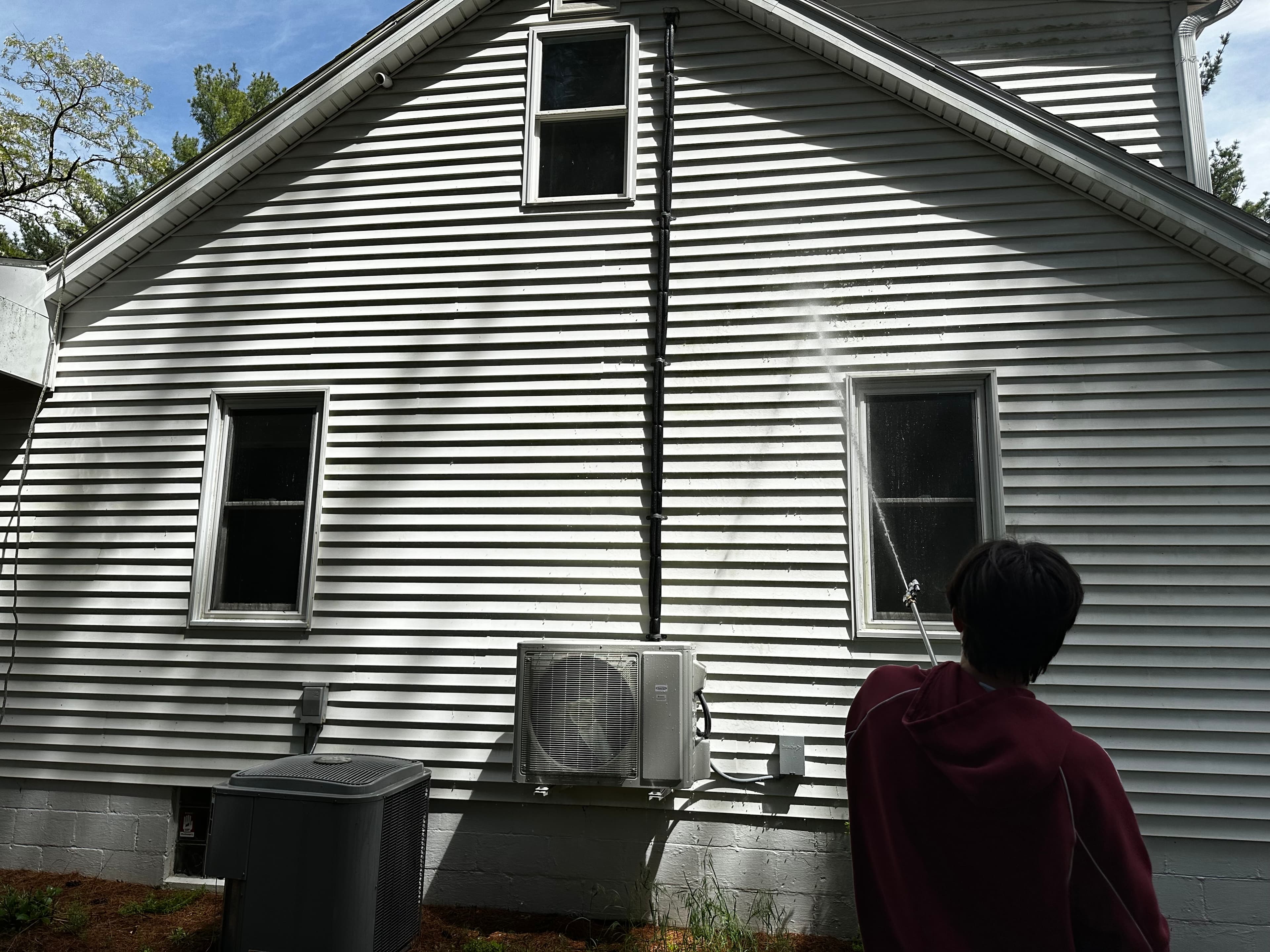 Person pressure washing white siding in Wheatfield, Indiana, showcasing the removal of grime and restoration of brightness.