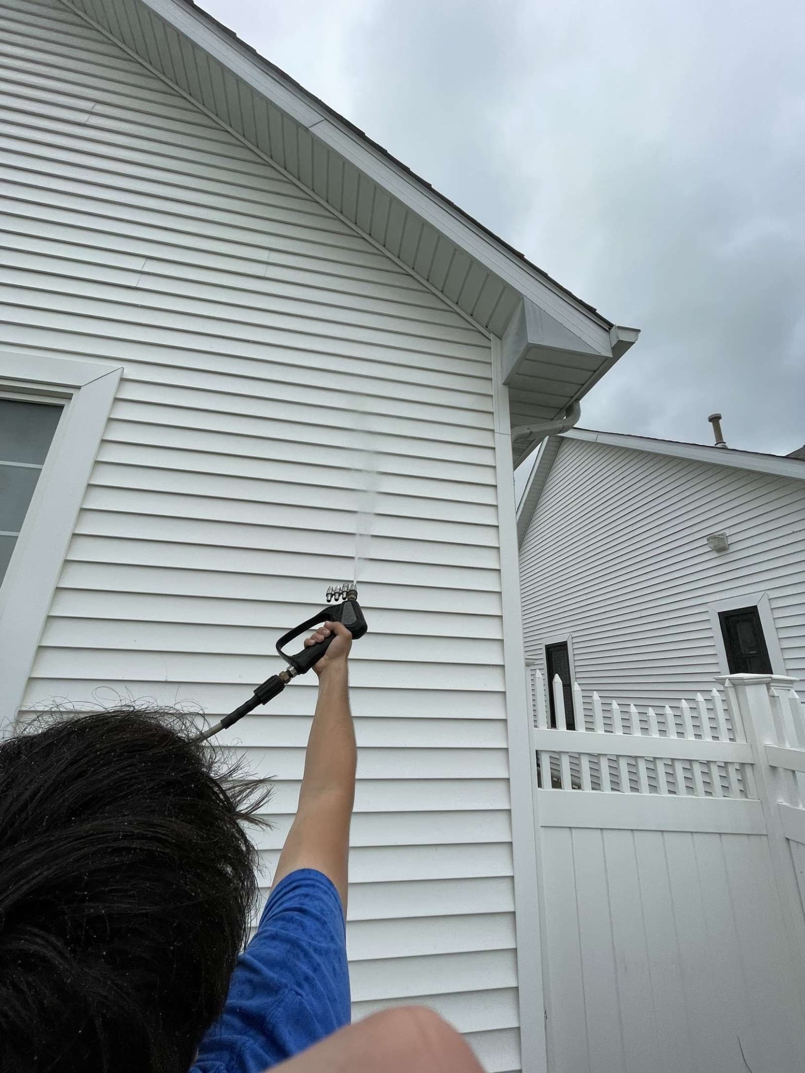 Person pressure washing white vinyl siding on house
