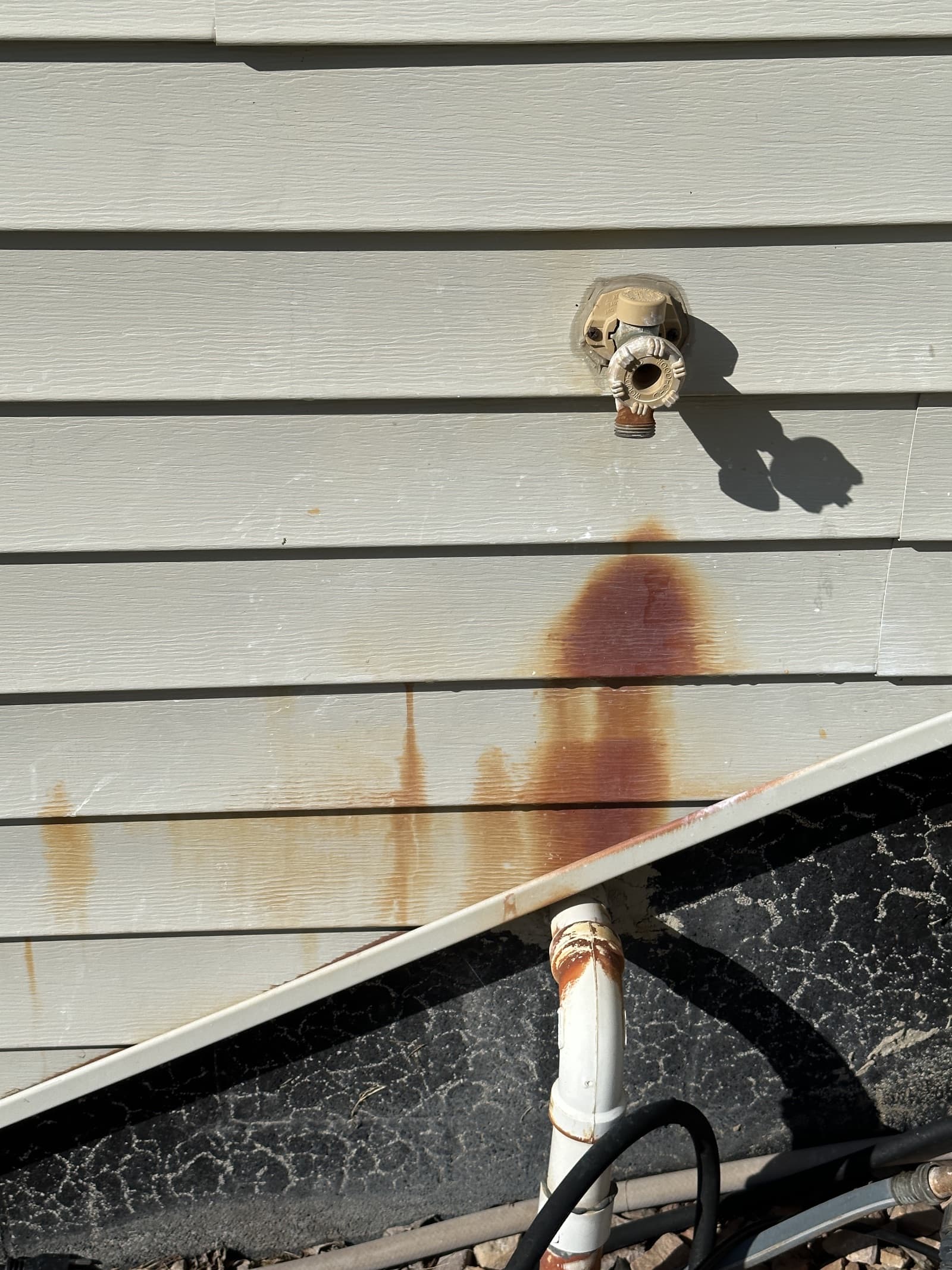Rust stains on beige vinyl siding near outdoor faucet
