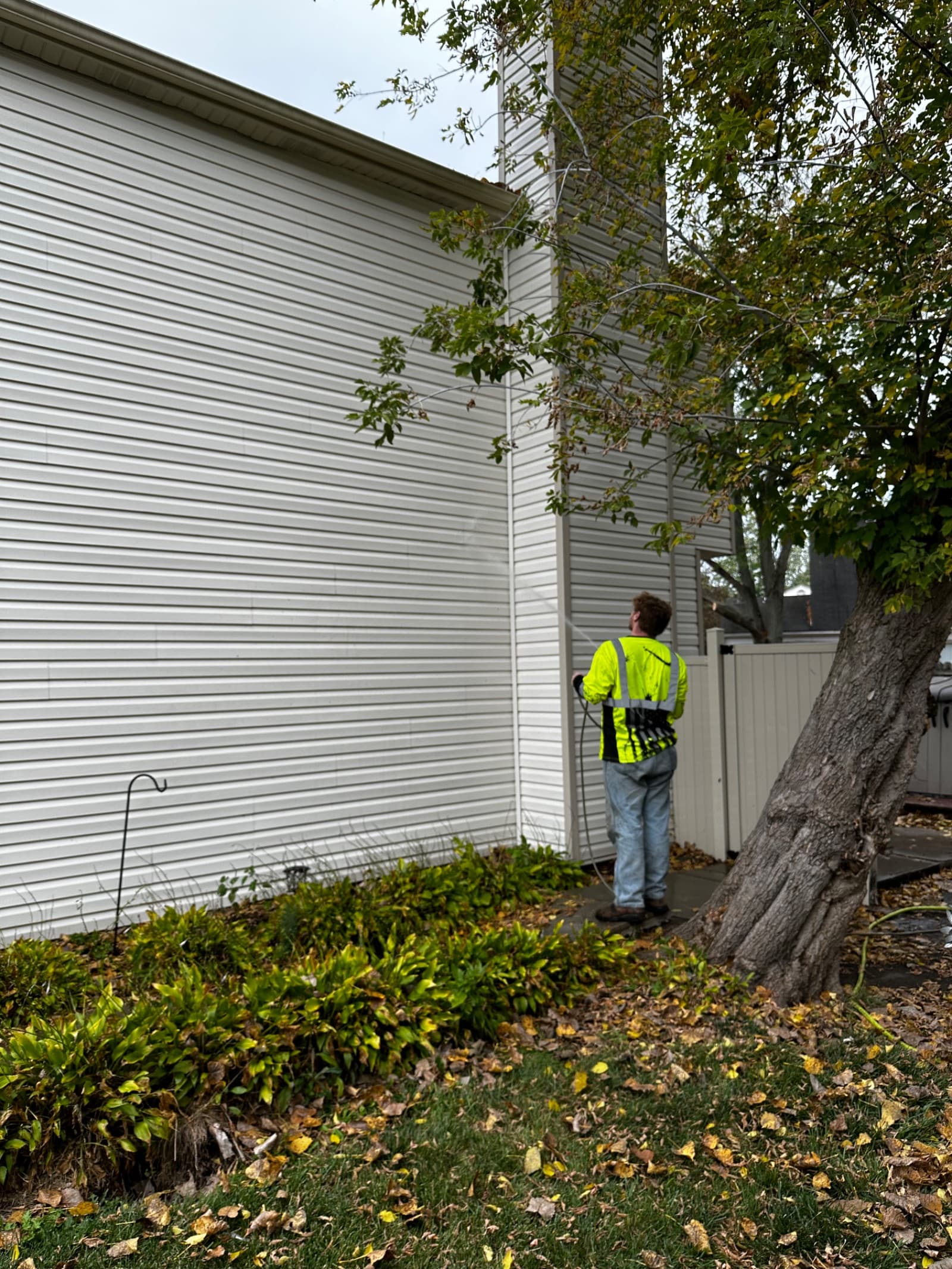 Technician pressure washing white vinyl siding of house
