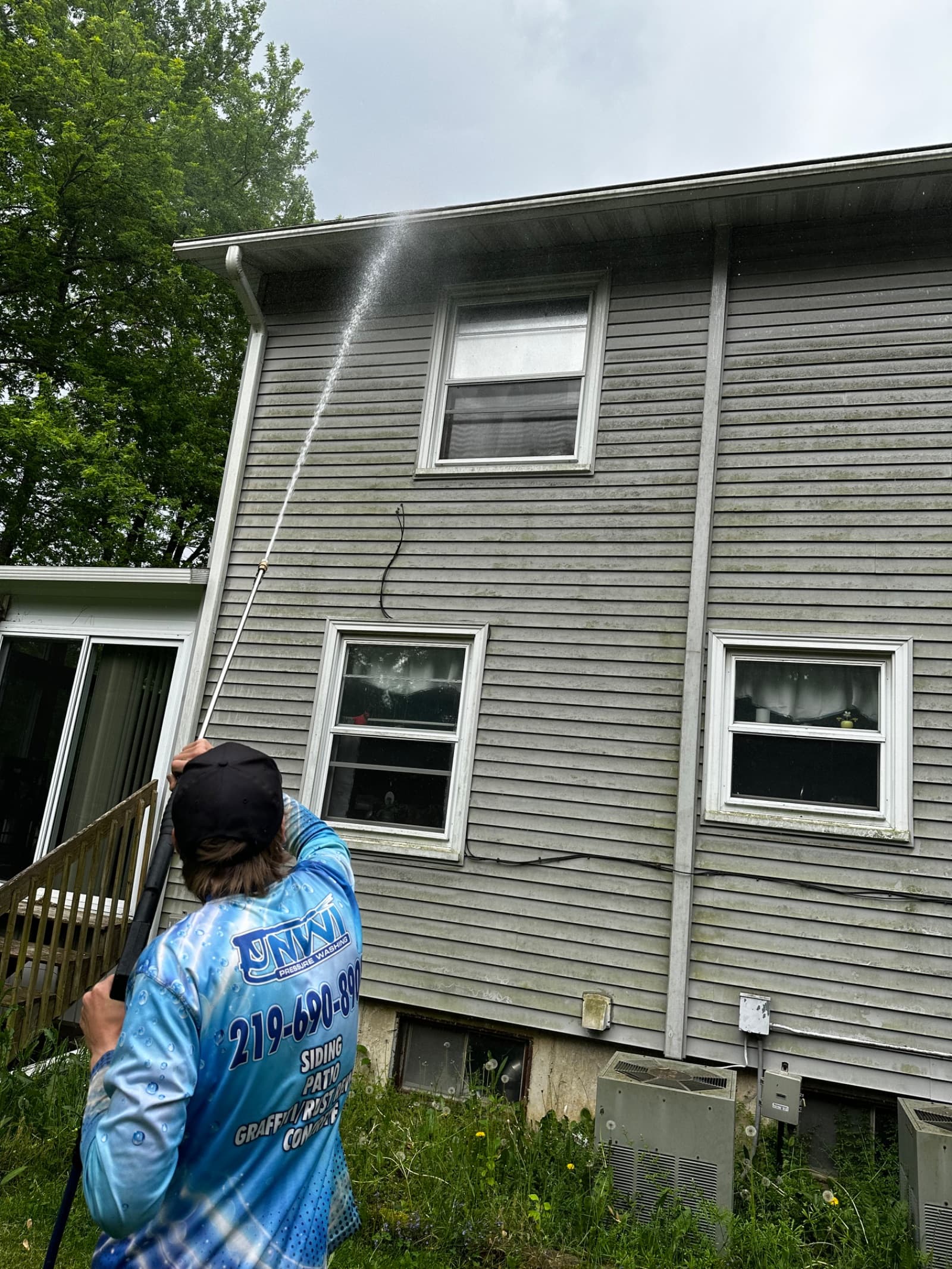 Technician pressure washing gray vinyl siding on two-story house