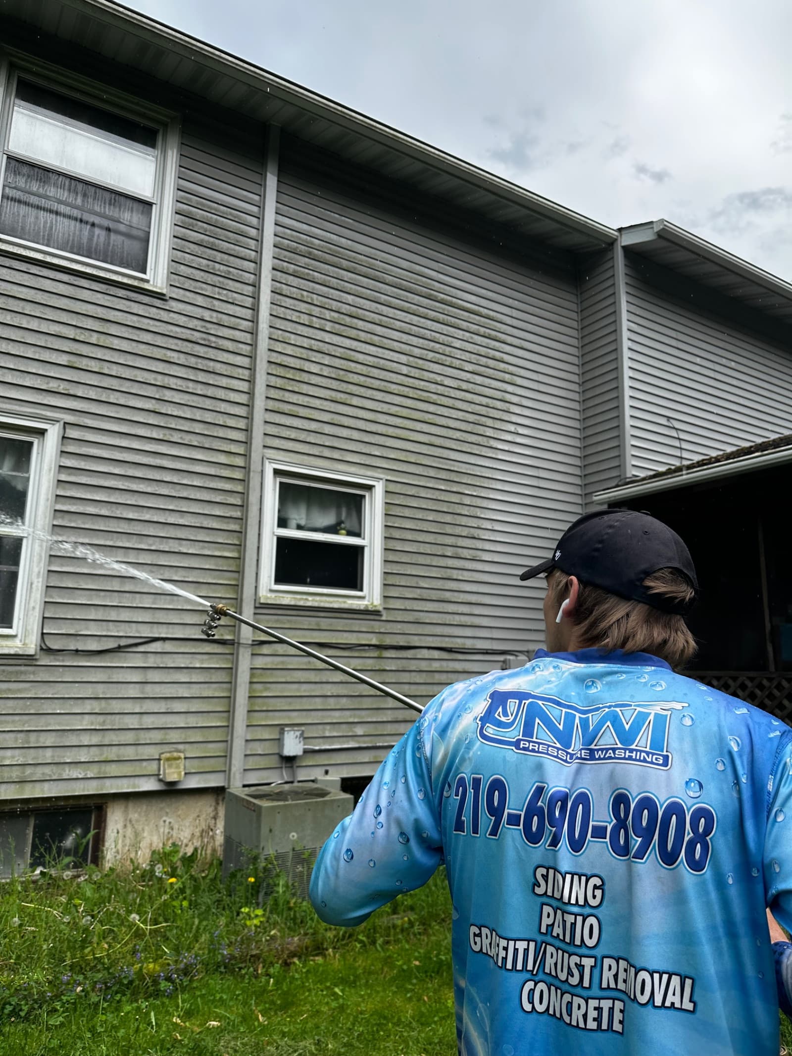 Technician pressure washing gray vinyl siding on house