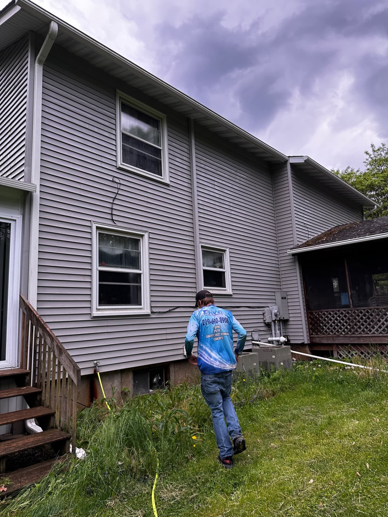 Man inspecting vinyl siding on a two-story house under cloudy sky