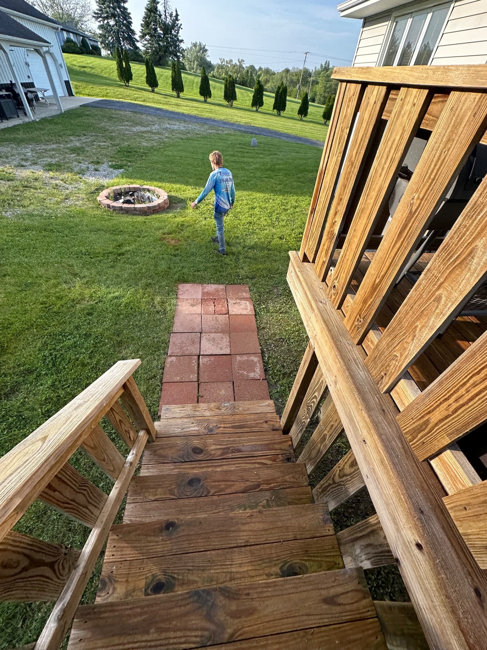 Wooden deck stairs leading to a brick path in a backyard