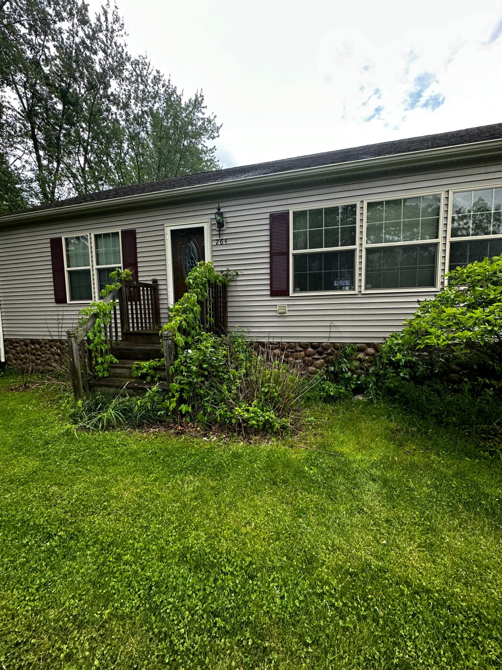Front view of house with vinyl siding and overgrown plants in Lowell, Indiana